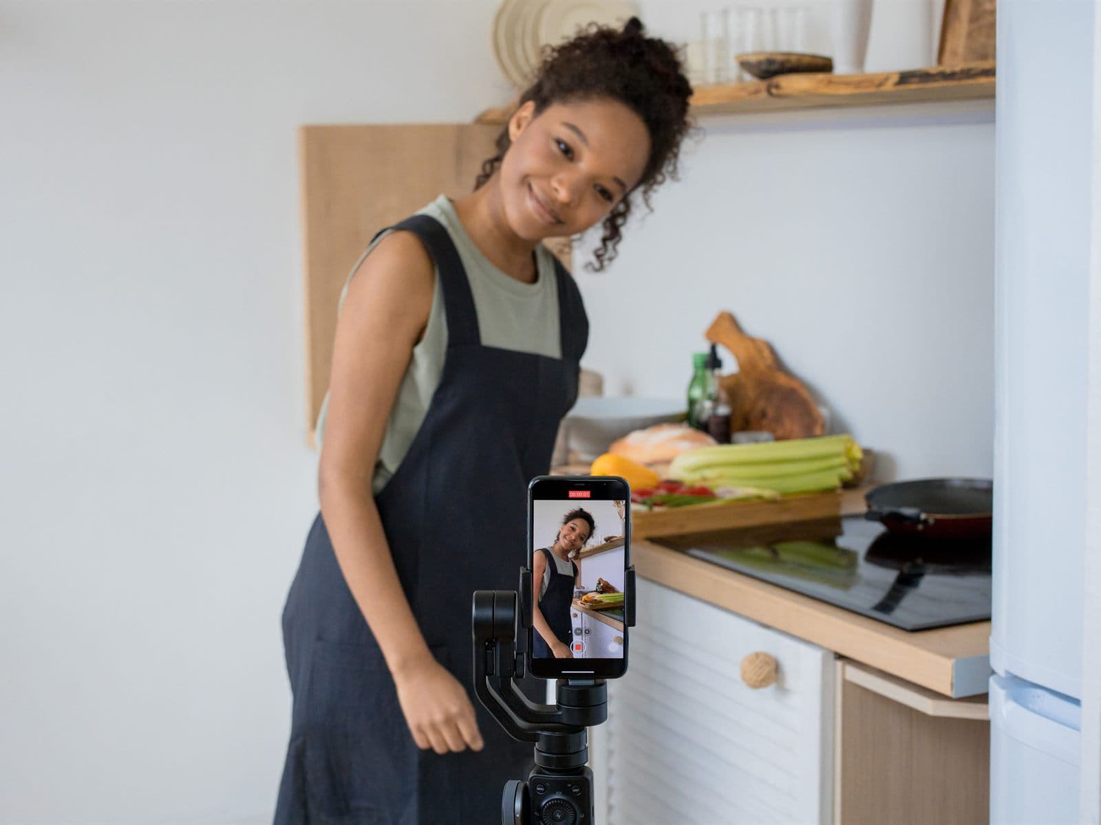 A content creator filming herself in a kitchen with a phone on a stabilizer
