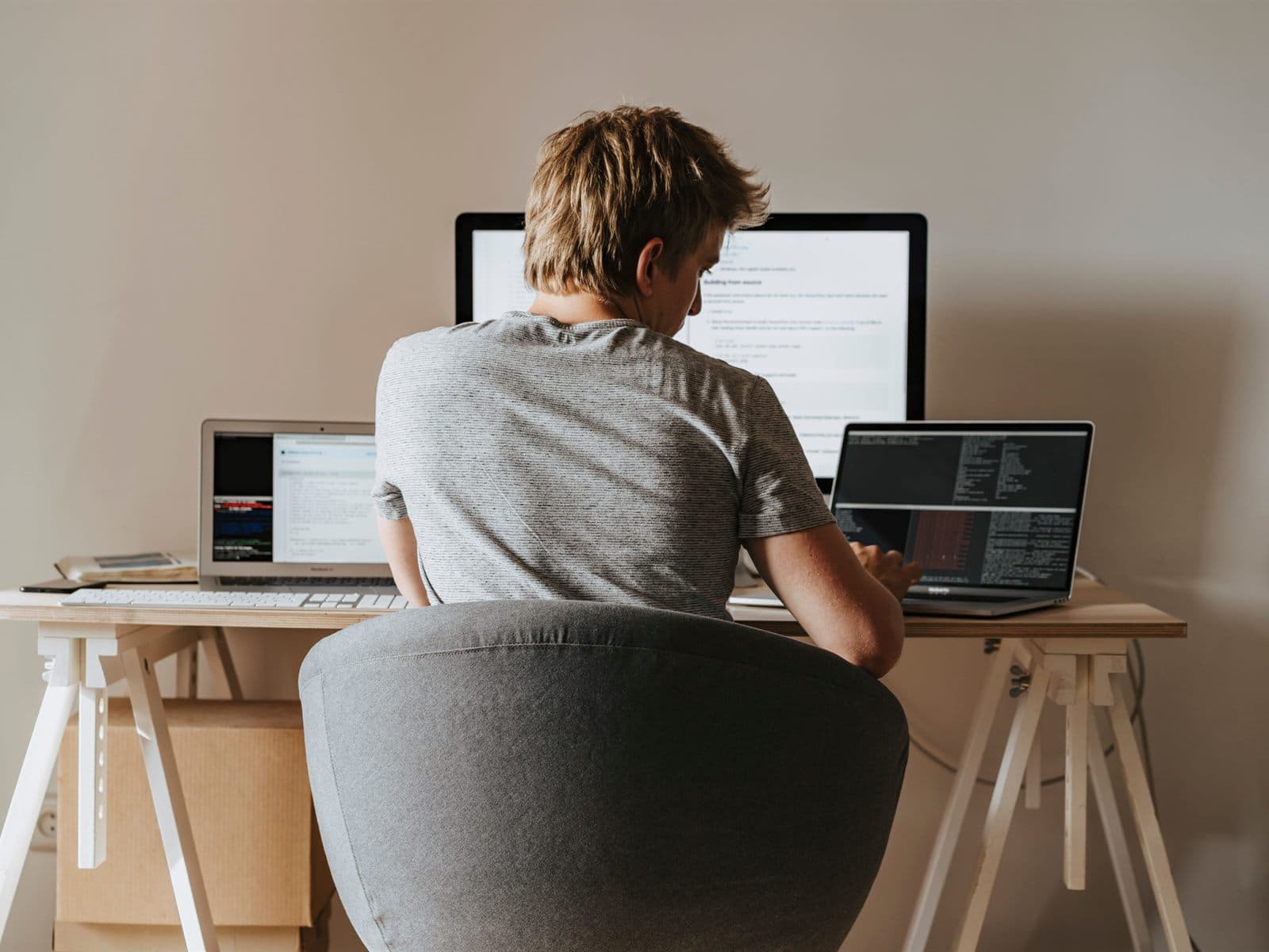 A freelancer working at a desk with a monitor and two laptops