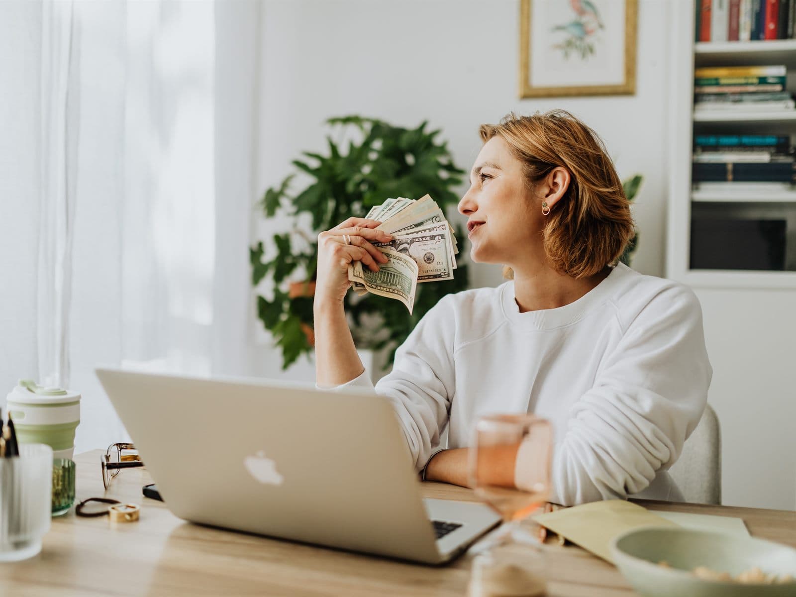 A woman at her laptop holding a fan of dollar bills